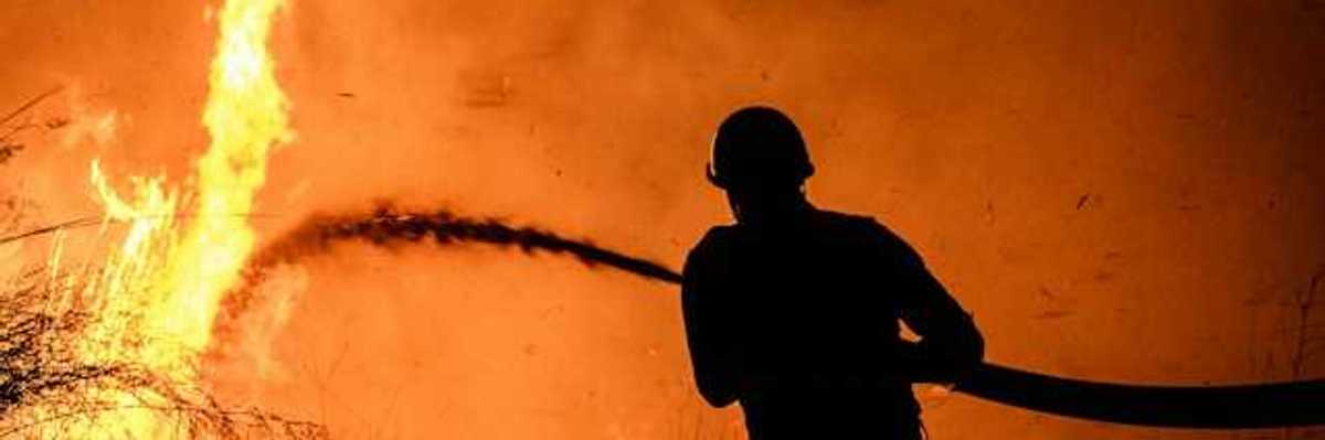 A silhouette of a firefighter spraying water on a wildfire