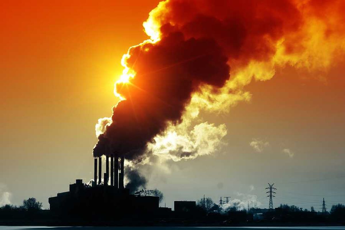 A silhouette of a power plant with billowing smoke and the sun in the background