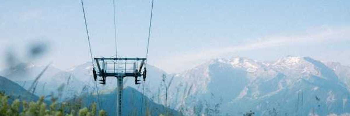 A ski run with green bushes growing under it and mountains the background