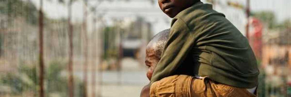 A small black boy sitting on his father's shoulders while looking into the camera