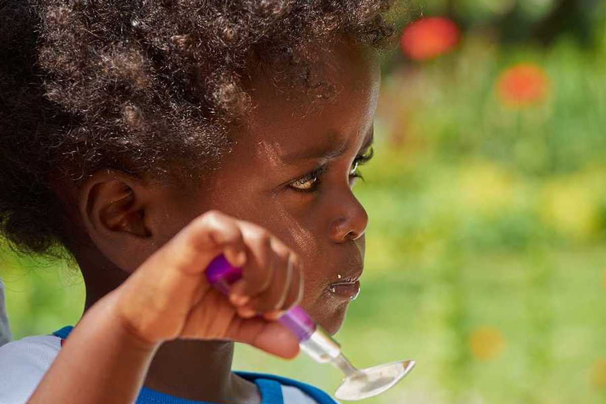 A small black child eating with a spoon