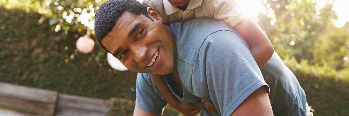 A small Black child riding on his father's back in a beautiful garden setting