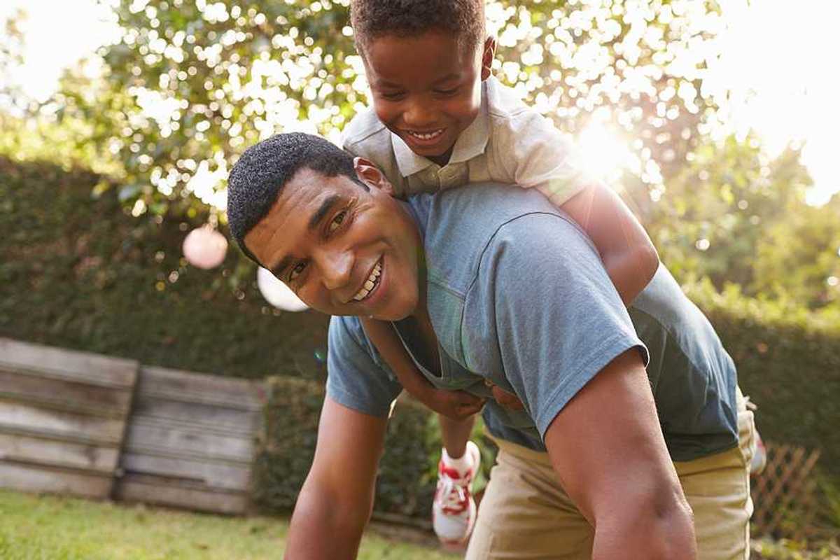 A small Black child riding on his father's back in a beautiful garden setting
