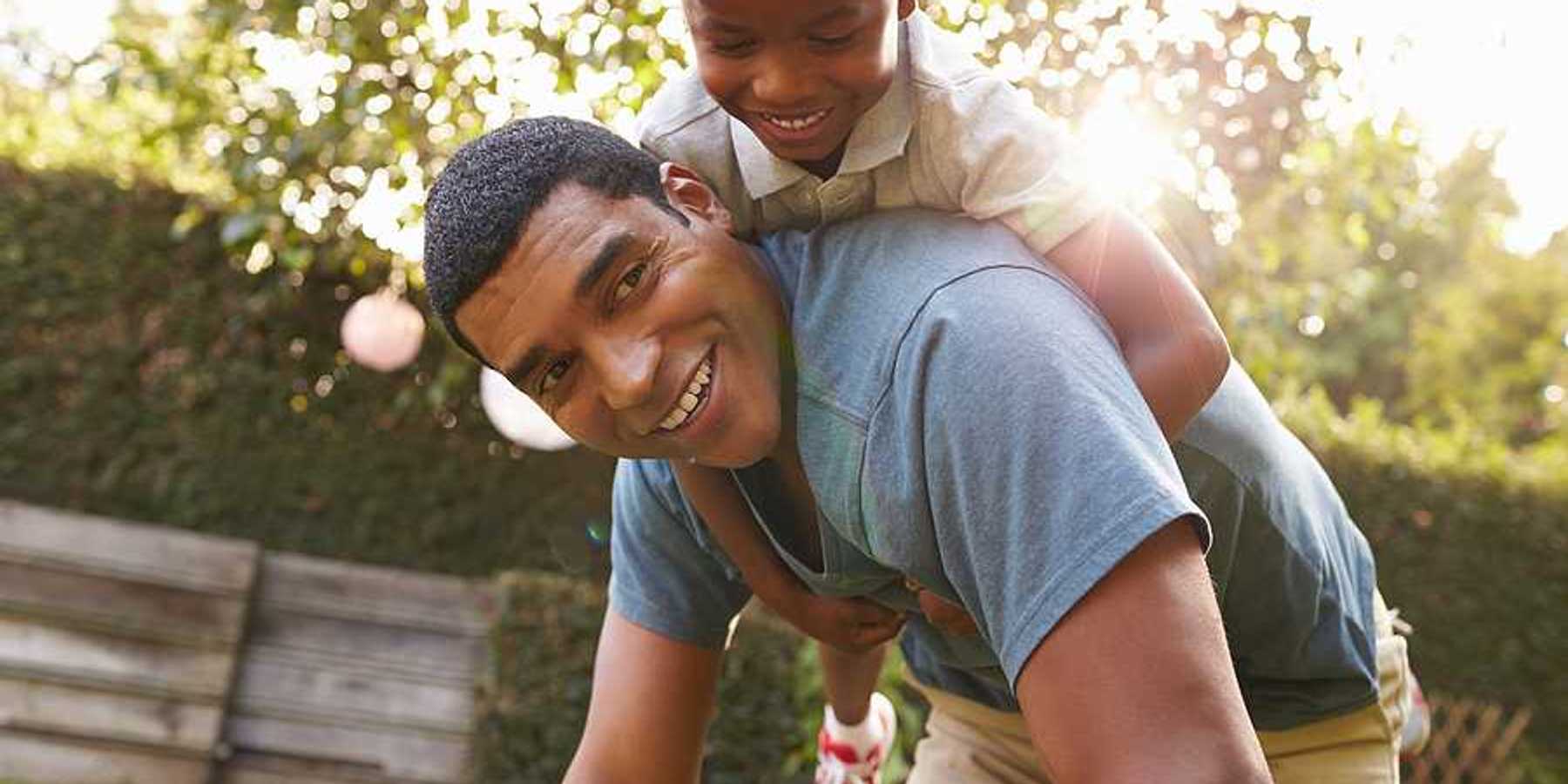 A small Black child riding on his father's back in a beautiful garden setting