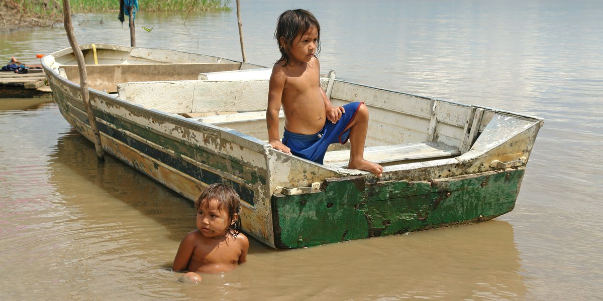 A small child in a boat on a river, with another child sitting in the water.