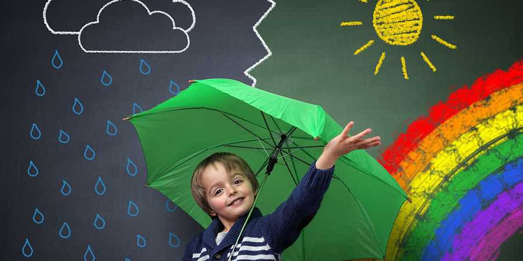 A small child under a green umbrella against a chalkboard with a rainbow and sun and rain on it