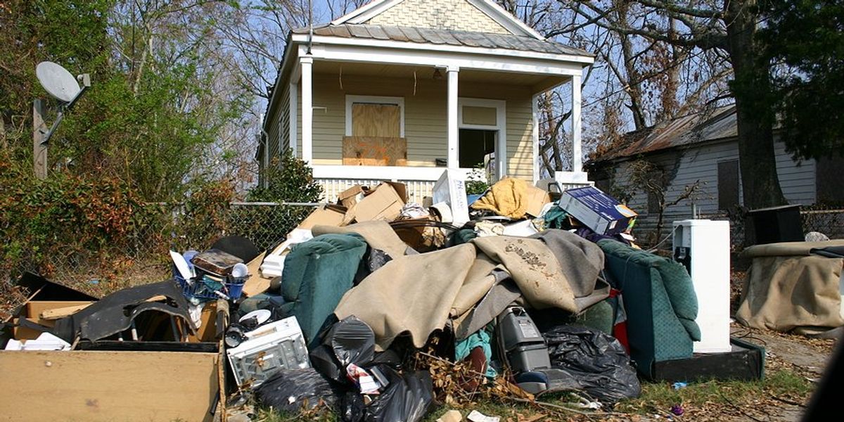 A small home with boarded windows and flood-damaged personal effects piled on the sidewalk