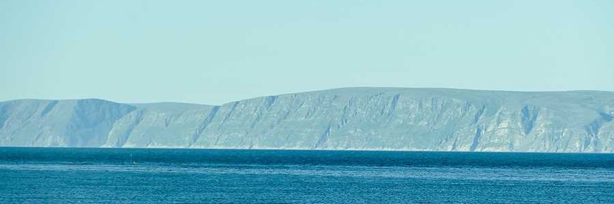 A small house on the edge of the water with mountains in the background