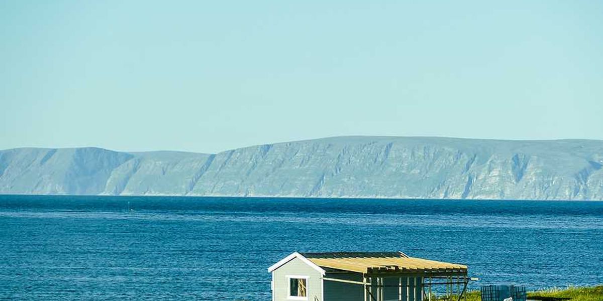 A small house on the edge of the water with mountains in the background