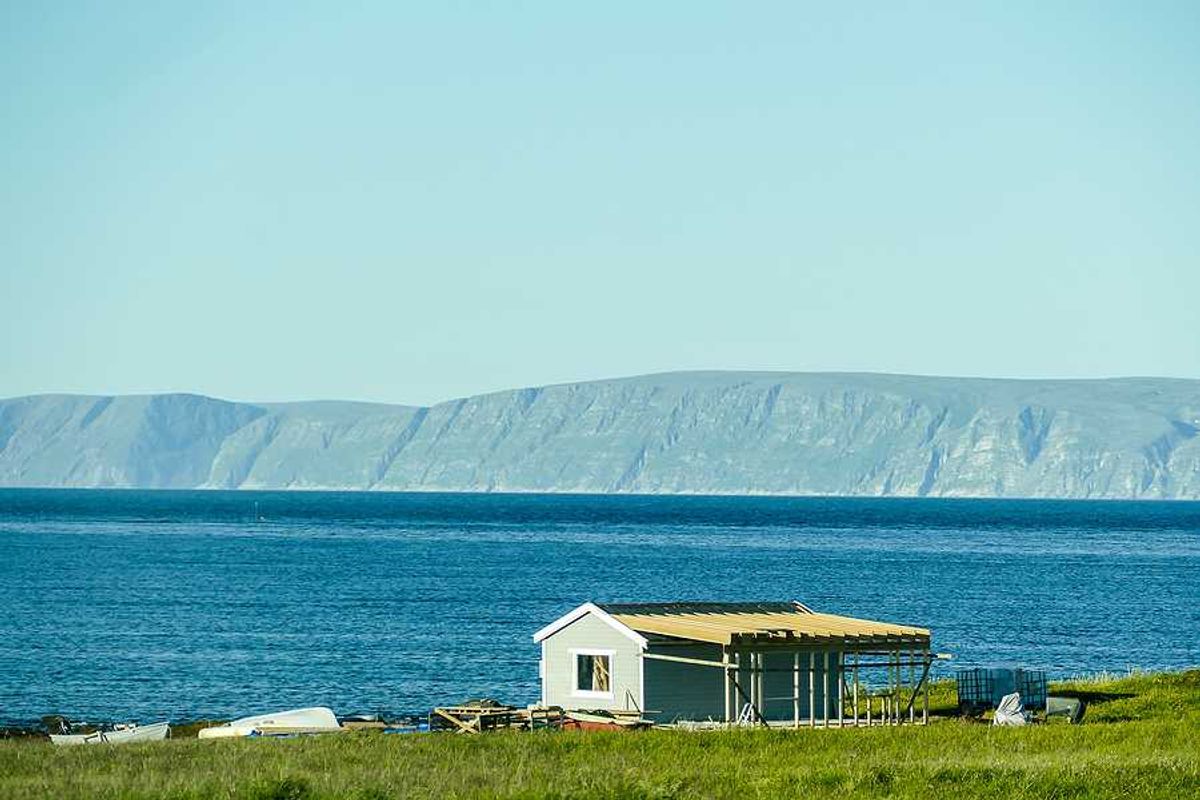 A small house on the edge of the water with mountains in the background
