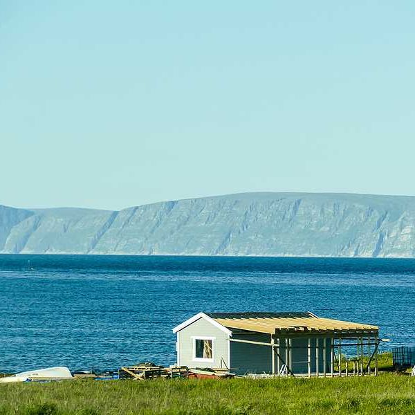 A small house on the edge of the water with mountains in the background