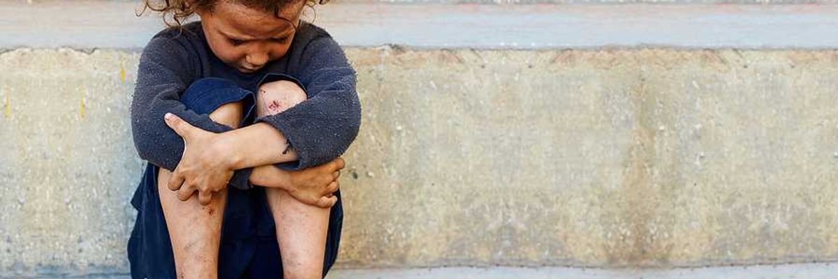 A small impoverished child sitting against a concrete curb