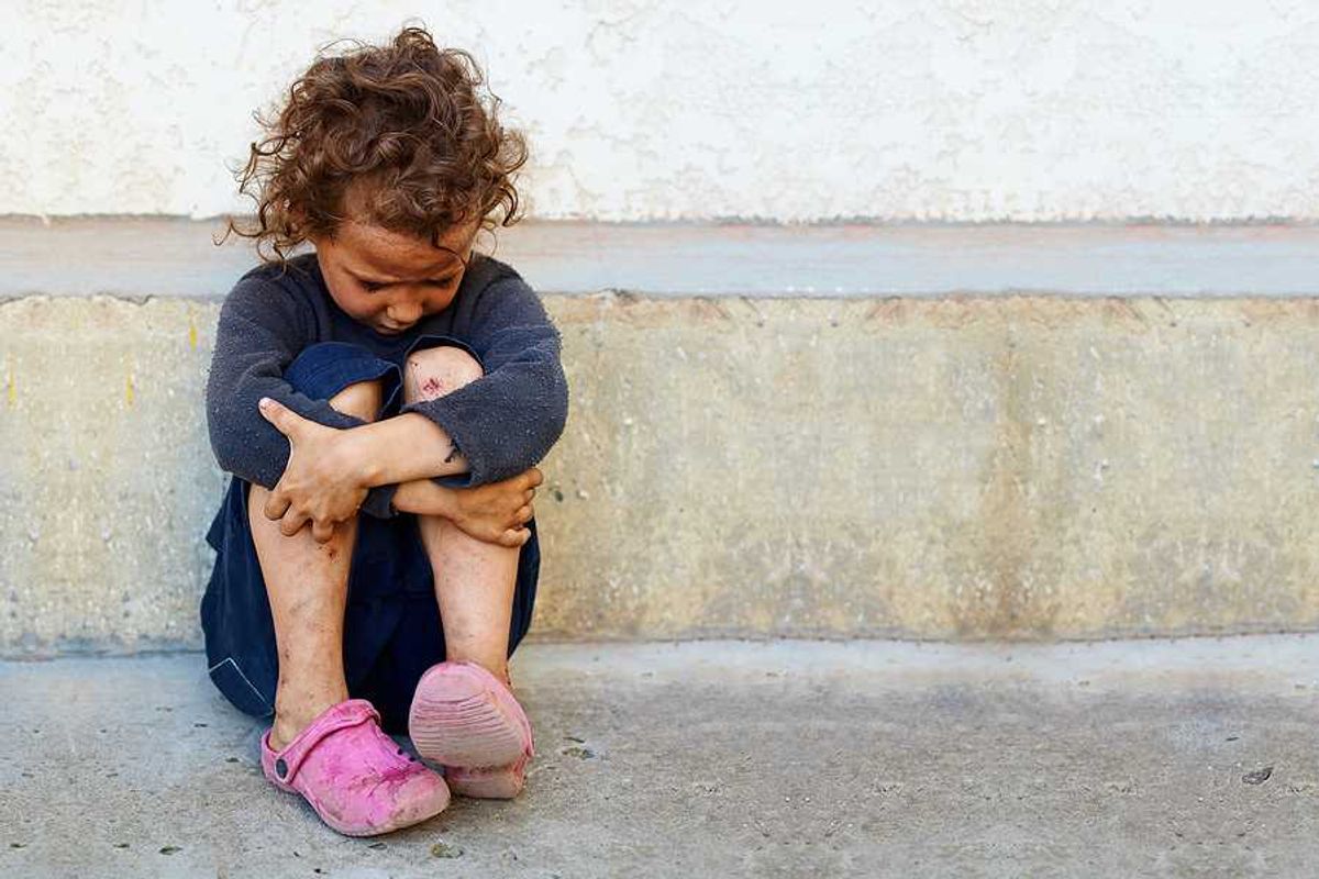 A small impoverished child sitting against a concrete curb
