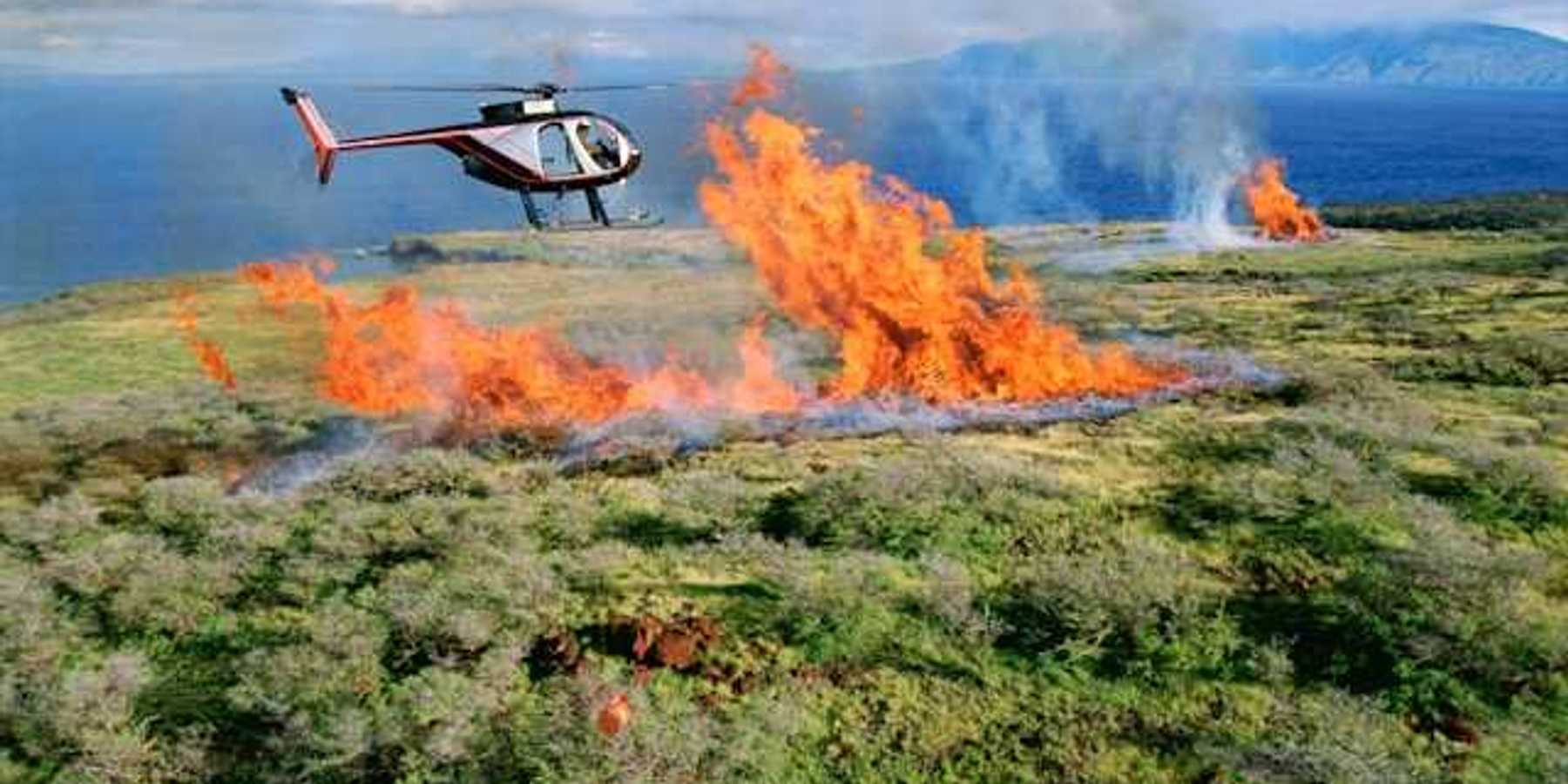 A small wildfire on a mountain with a helicopter flying overhead