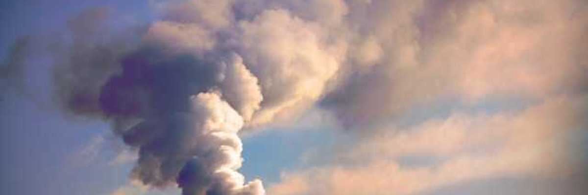 A smoke stack with smoke billowing out into the clouds