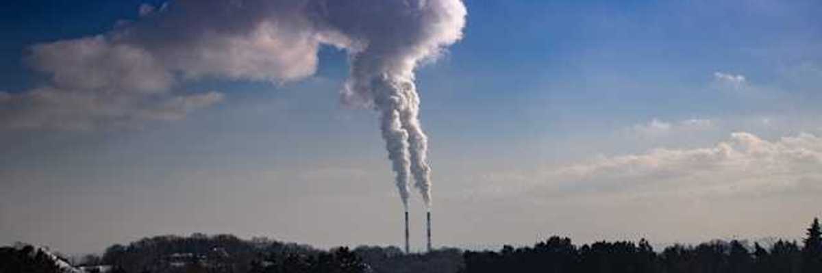 A snowy landscape with two smokestacks emitting pollution in the background