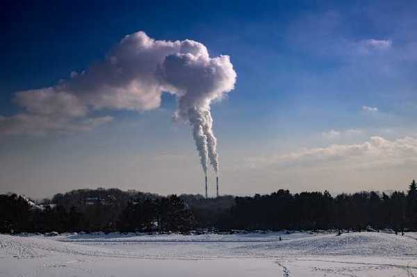 A snowy landscape with two smokestacks emitting pollution in the background