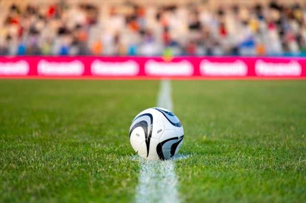 A soccer ball on green grass with people seated in bleachers in the background