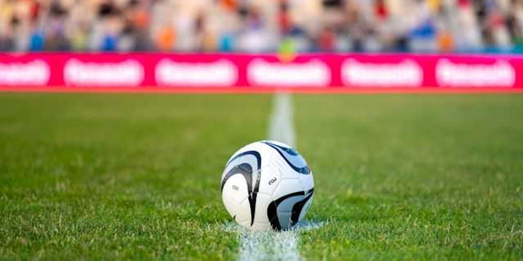 A soccer ball on green grass with people seated in bleachers in the background