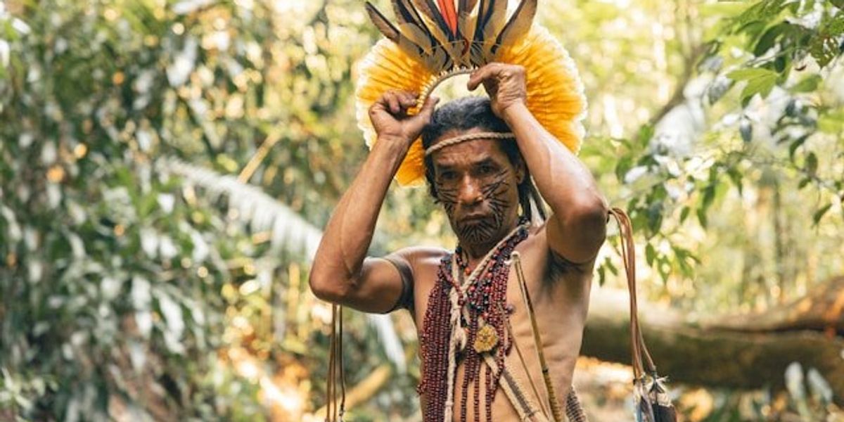 A South American indigenous man placing a headdress on his head.