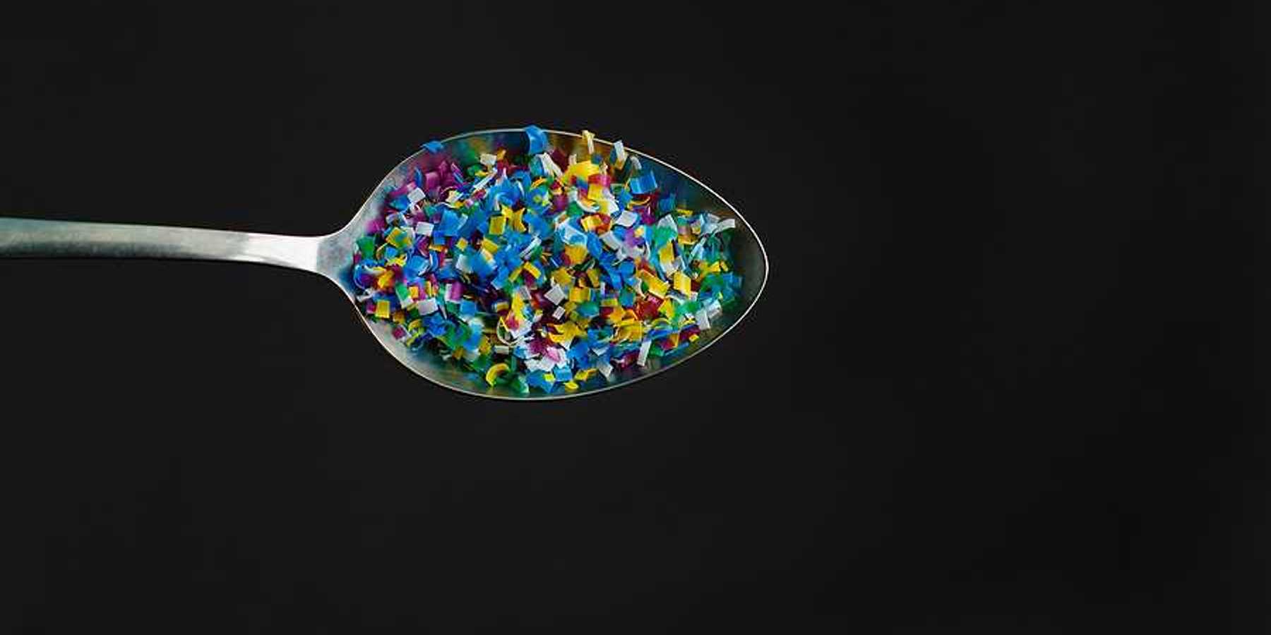 A spoon with microplastics in it on a black background