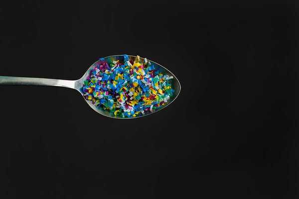A spoon with microplastics in it on a black background