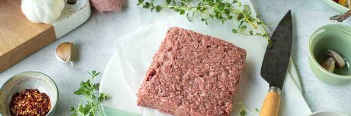 A square slab of real or vegan meat on a surface surrounded by spices