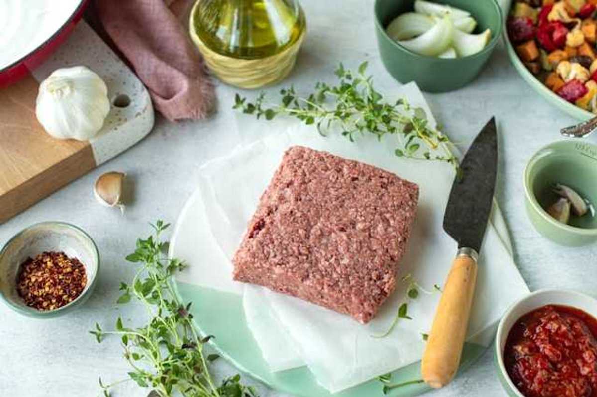 A square slab of real or vegan meat on a surface surrounded by spices