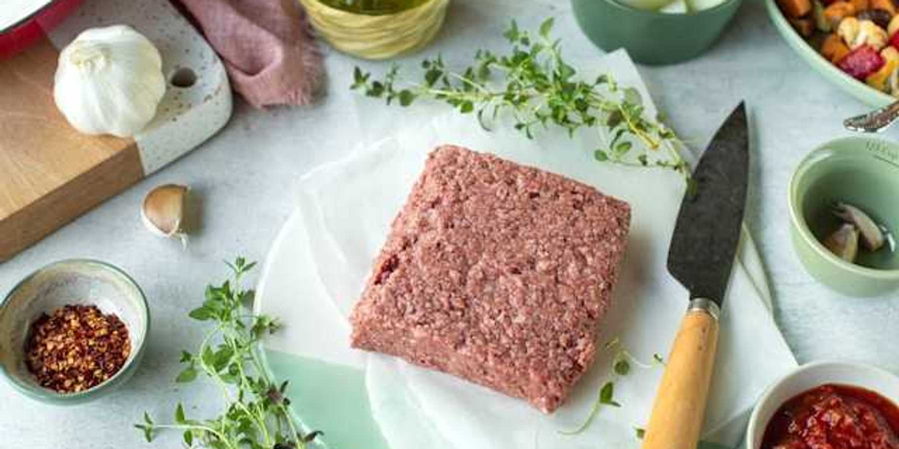 A square slab of real or vegan meat on a surface surrounded by spices