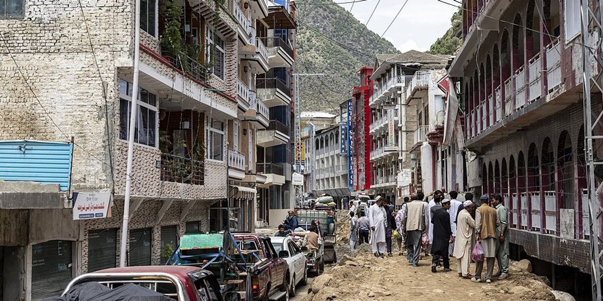 A street in Pakistan in the aftermath of a flood with people walking to one side and cars to the other.