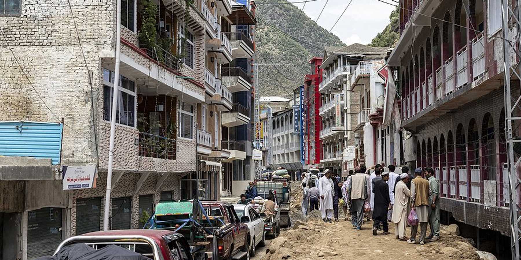 A street in Pakistan in the aftermath of a flood with people walking to one side and cars to the other.
