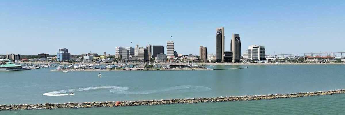 A sunny aerial view of downtown Corpus Christi, Texas, with the sparkling bay in the foreground and boats cruising through the water.