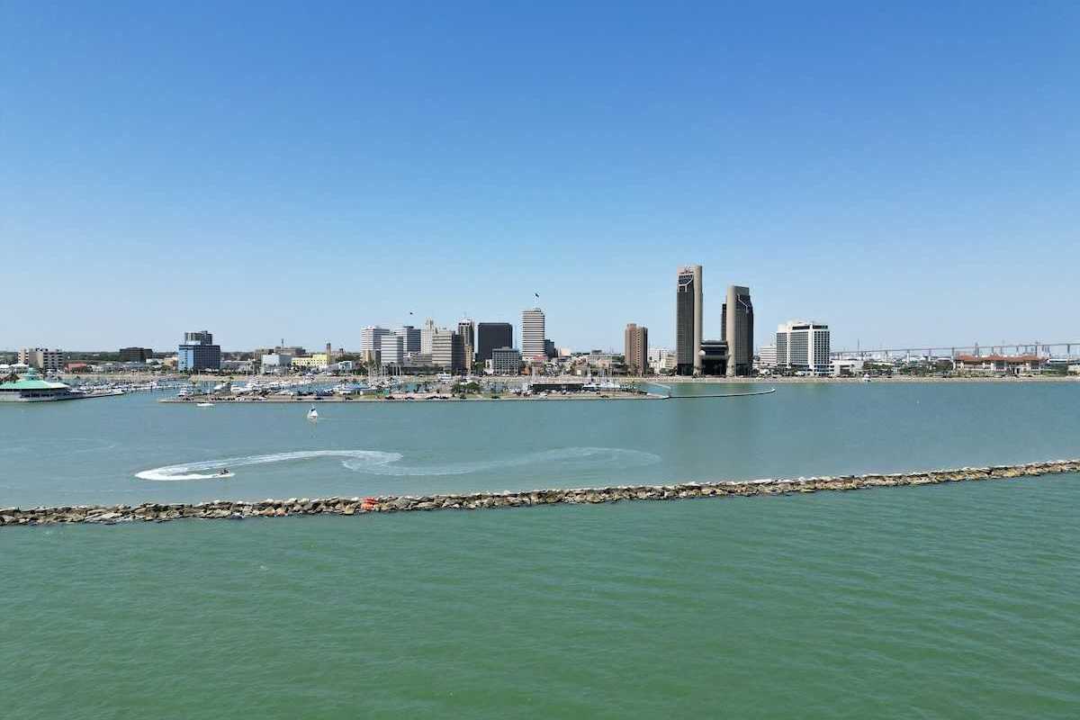 A sunny aerial view of downtown Corpus Christi, Texas, with the sparkling bay in the foreground and boats cruising through the water.