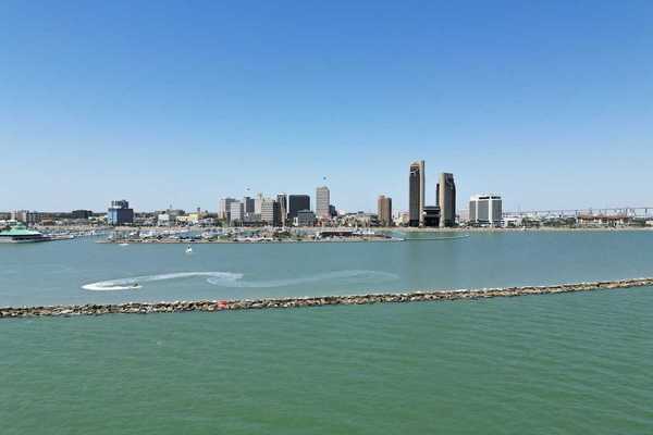 A sunny aerial view of downtown Corpus Christi, Texas, with the sparkling bay in the foreground and boats cruising through the water.