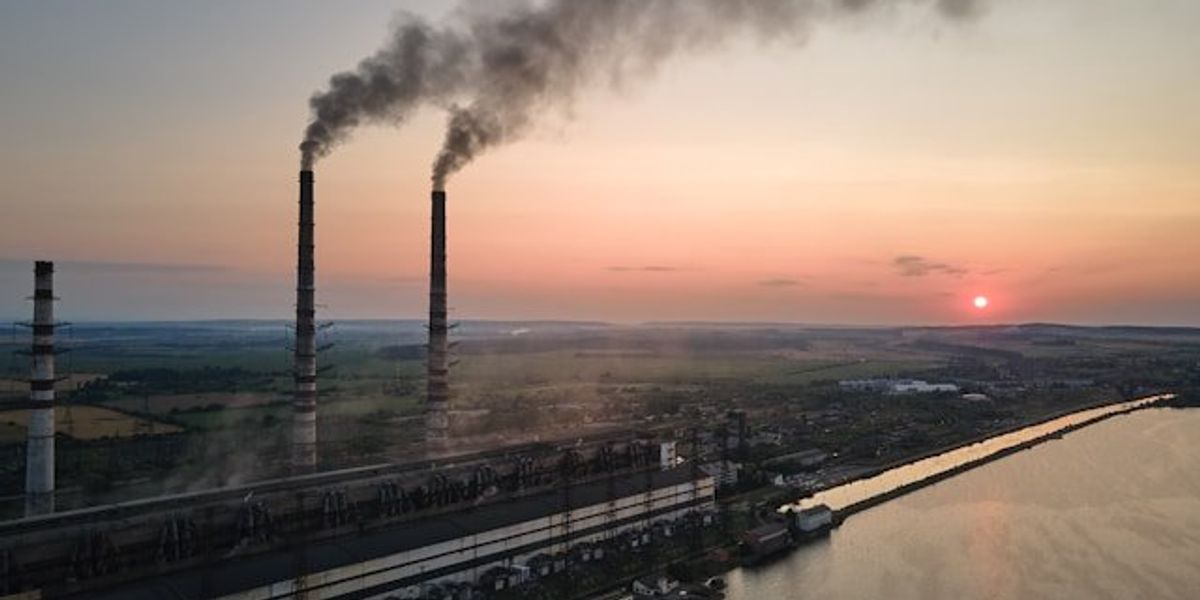 A sunset view of a factory with smokestacks billowing smoke.