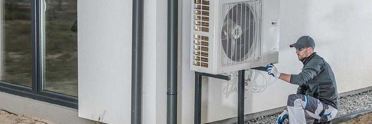 A technician working on a heat pump installed on the side of a home