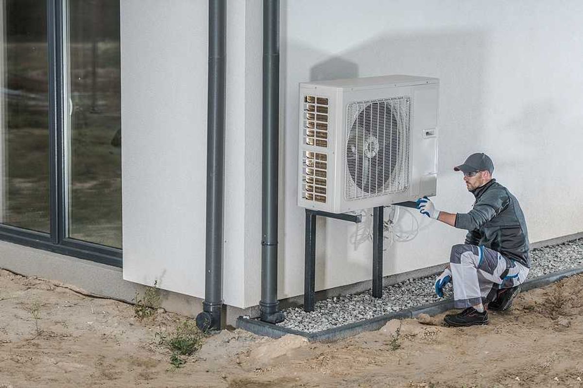 A technician working on a heat pump installed on the side of a home