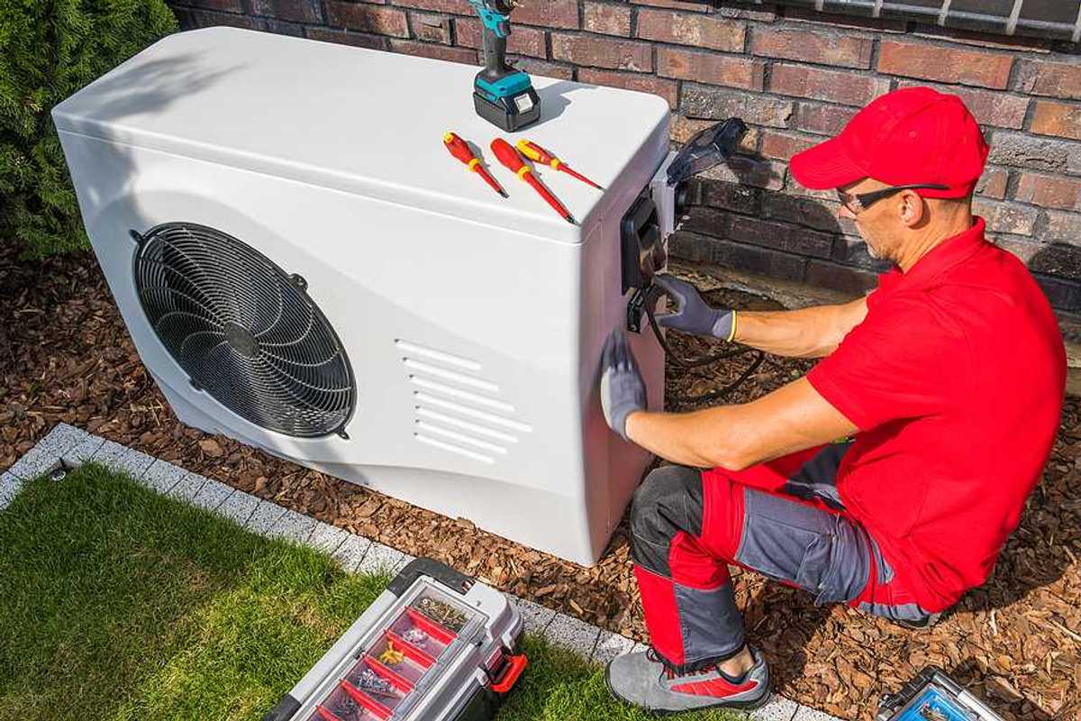 A technician working on a heat pump outside a house