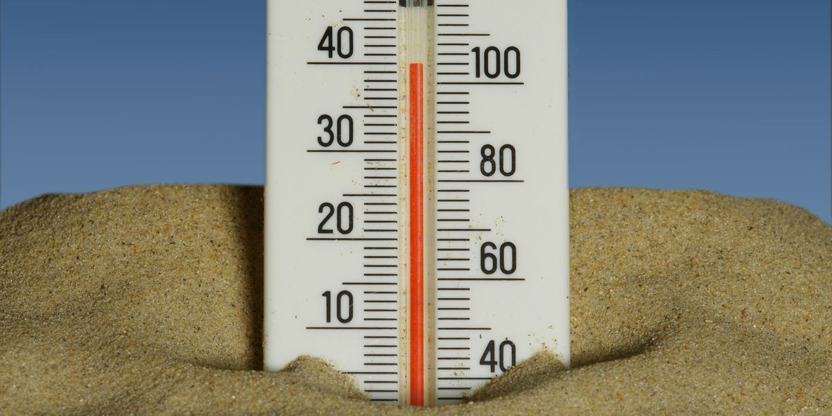 A thermometer in the sand showing temperatures near 40 degrees celsius with a blue sky in the background.