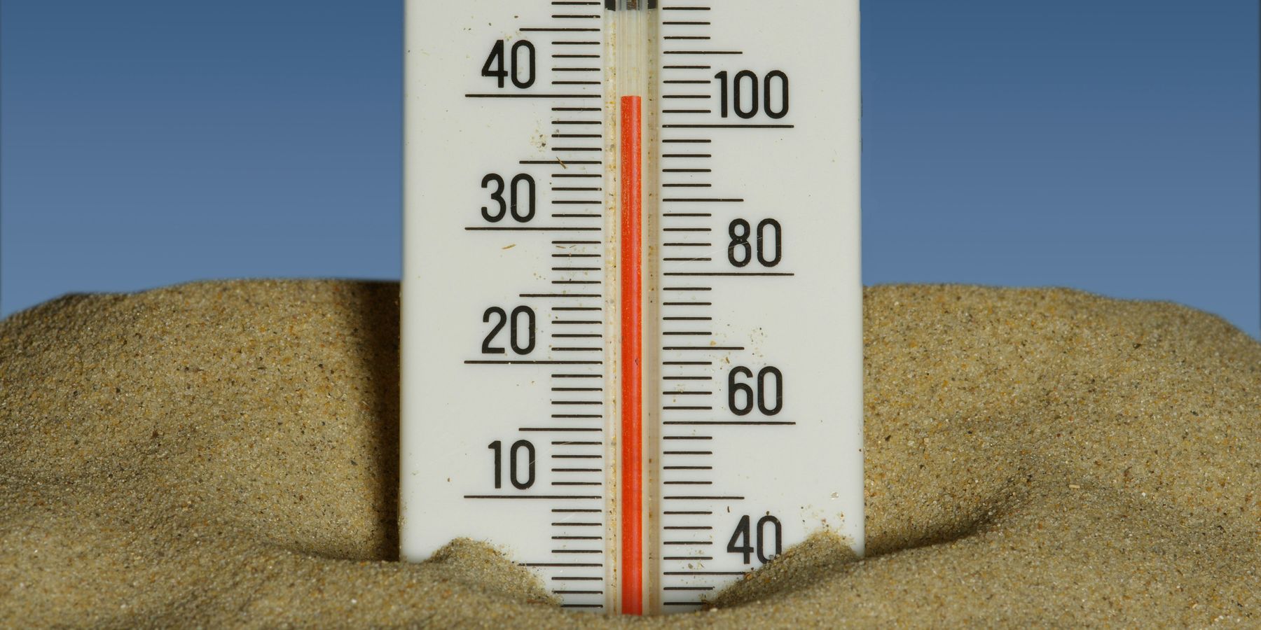 A thermometer in the sand showing temperatures near 40 degrees celsius with a blue sky in the background.