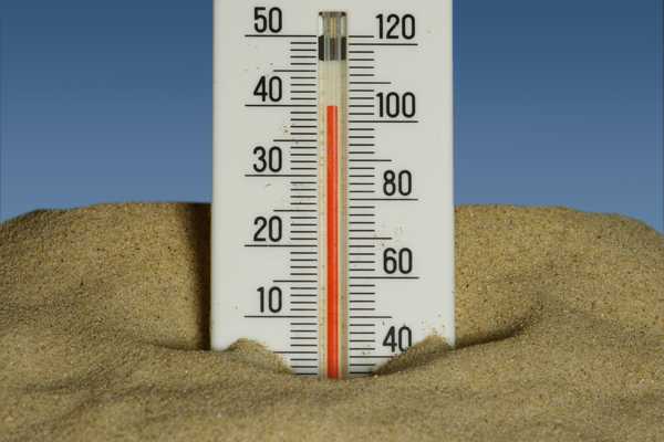A thermometer in the sand showing temperatures near 40 degrees celsius with a blue sky in the background.