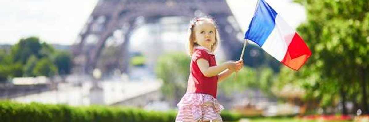 A toddler holding a French flag standing next to the Eiffel Tower in Paris