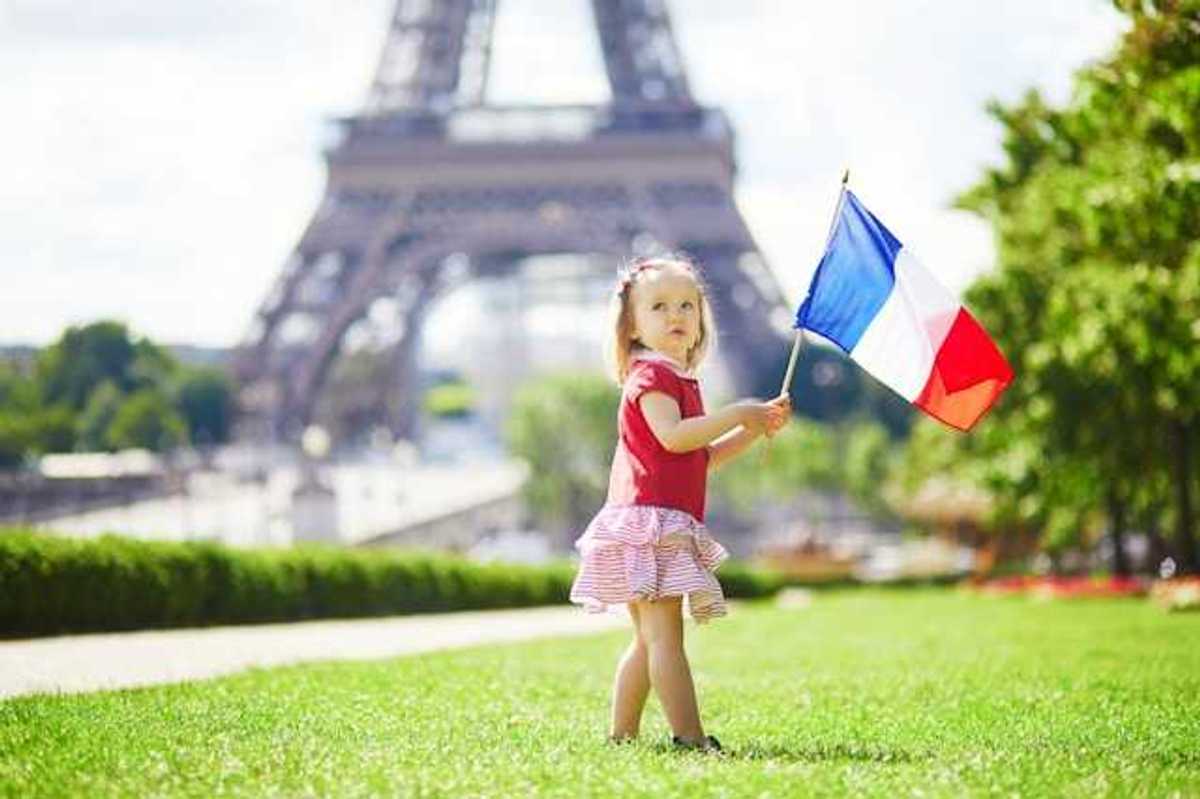 A toddler holding a French flag standing next to the Eiffel Tower in Paris