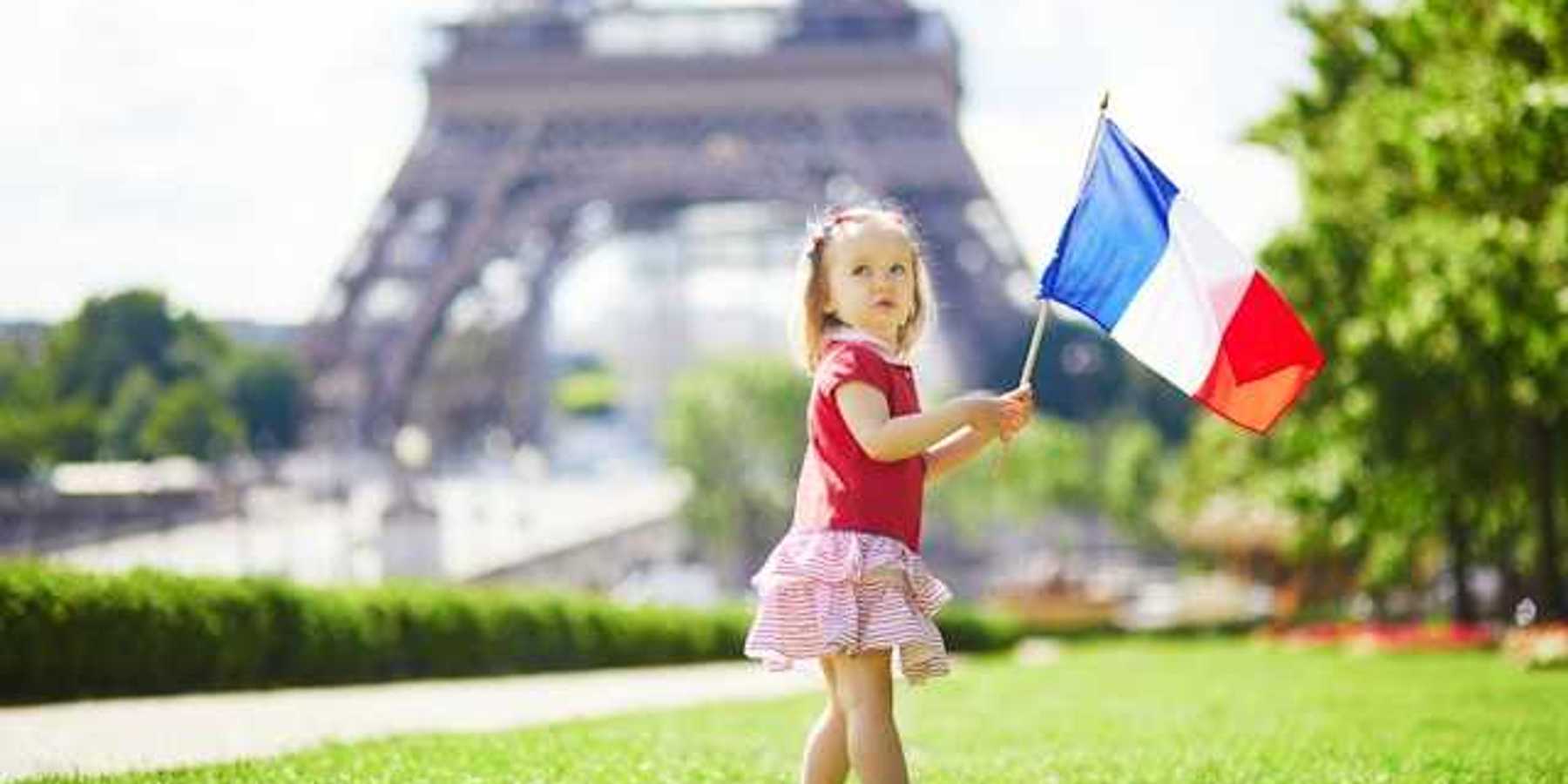 A toddler holding a French flag standing next to the Eiffel Tower in Paris