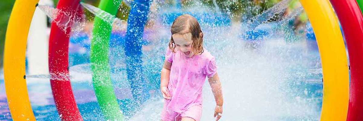 A toddler run through a multicolored fountain on a hot day