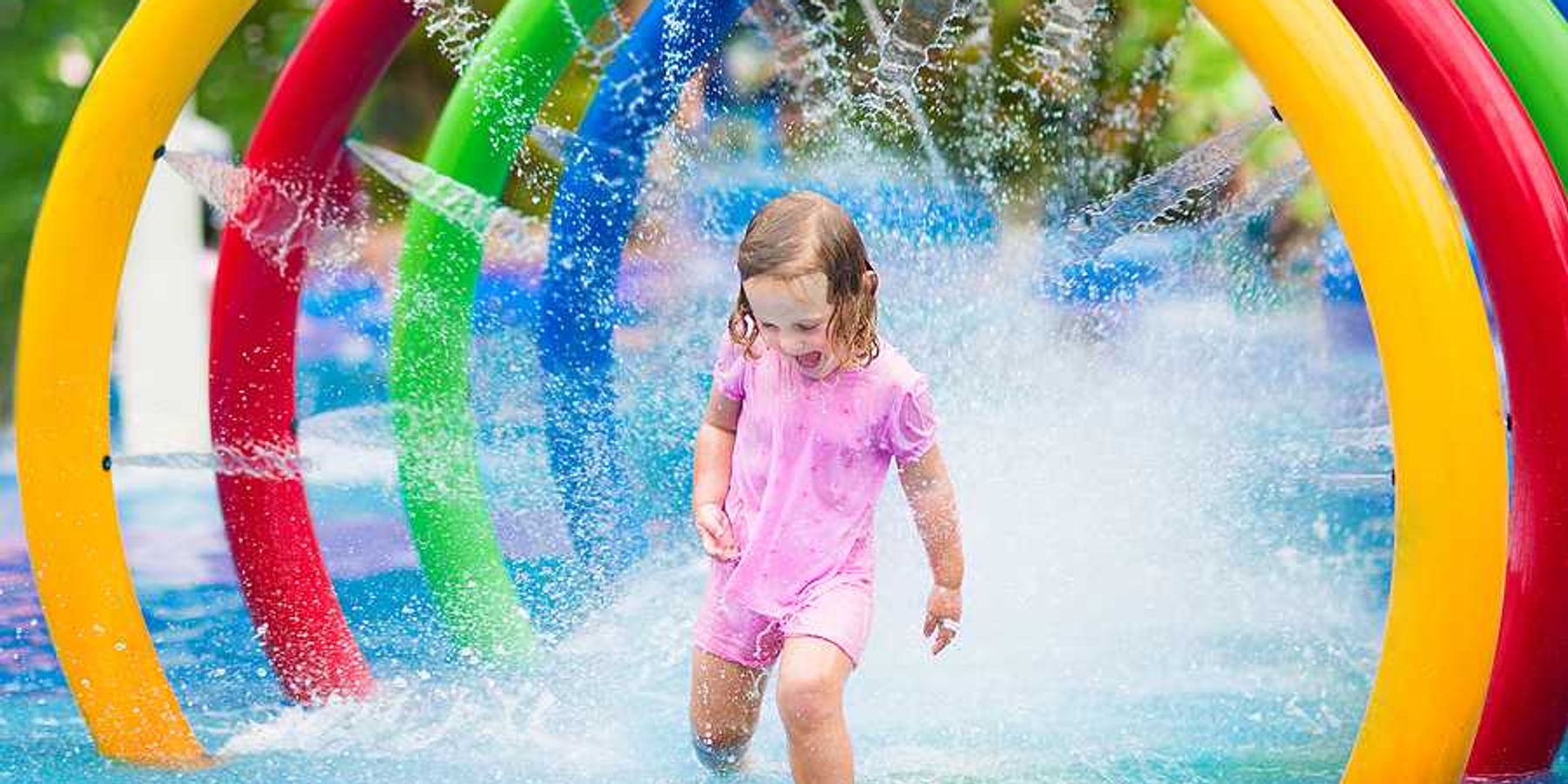 A toddler run through a multicolored fountain on a hot day