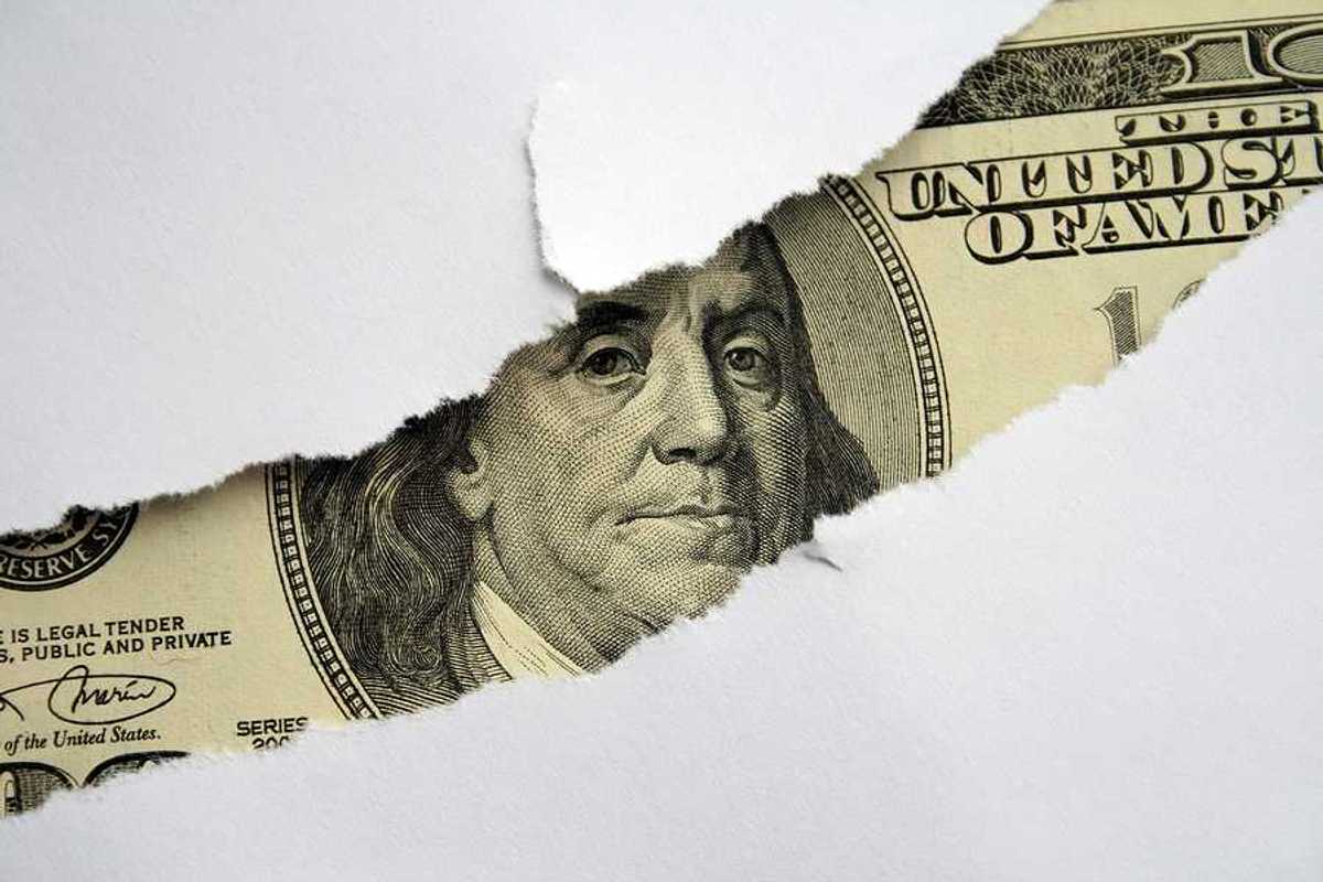 A torn white piece of paper with a $100 bill shown behind it