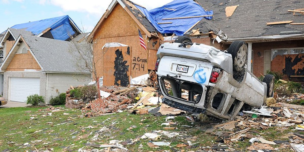 A tornado damaged house with an overturned car in the front yard.