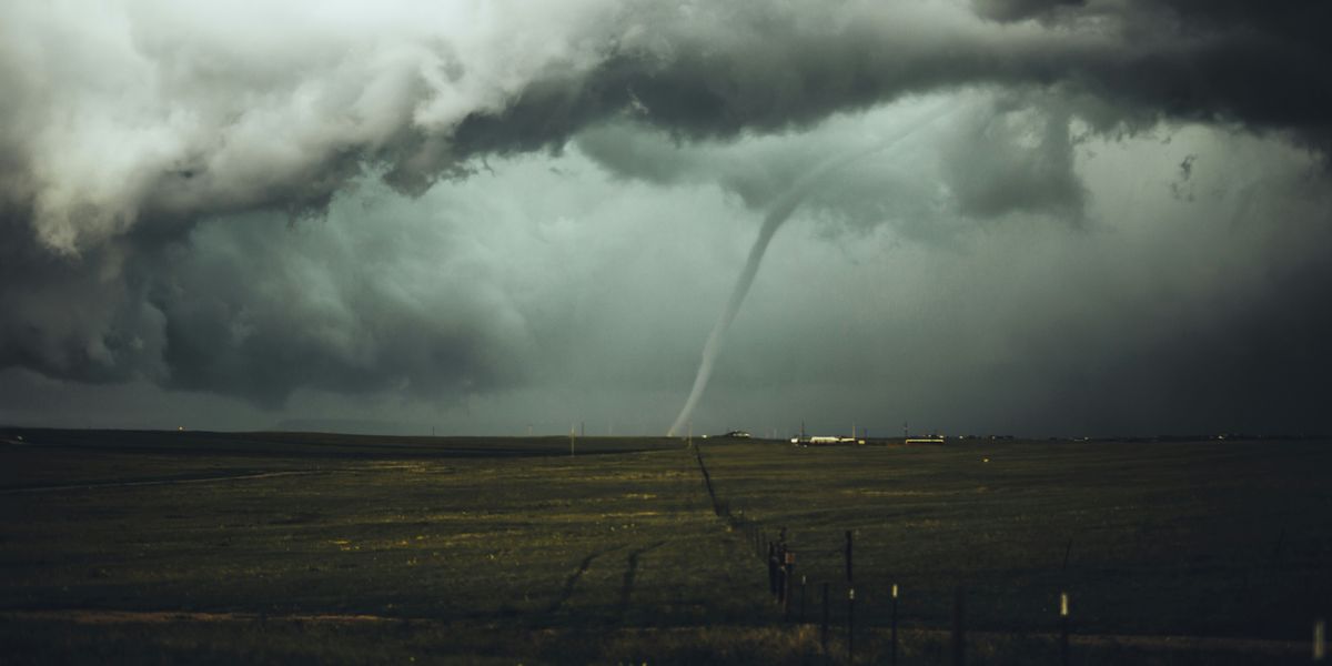 A tornado in the distance with green farm fields in the foreground.