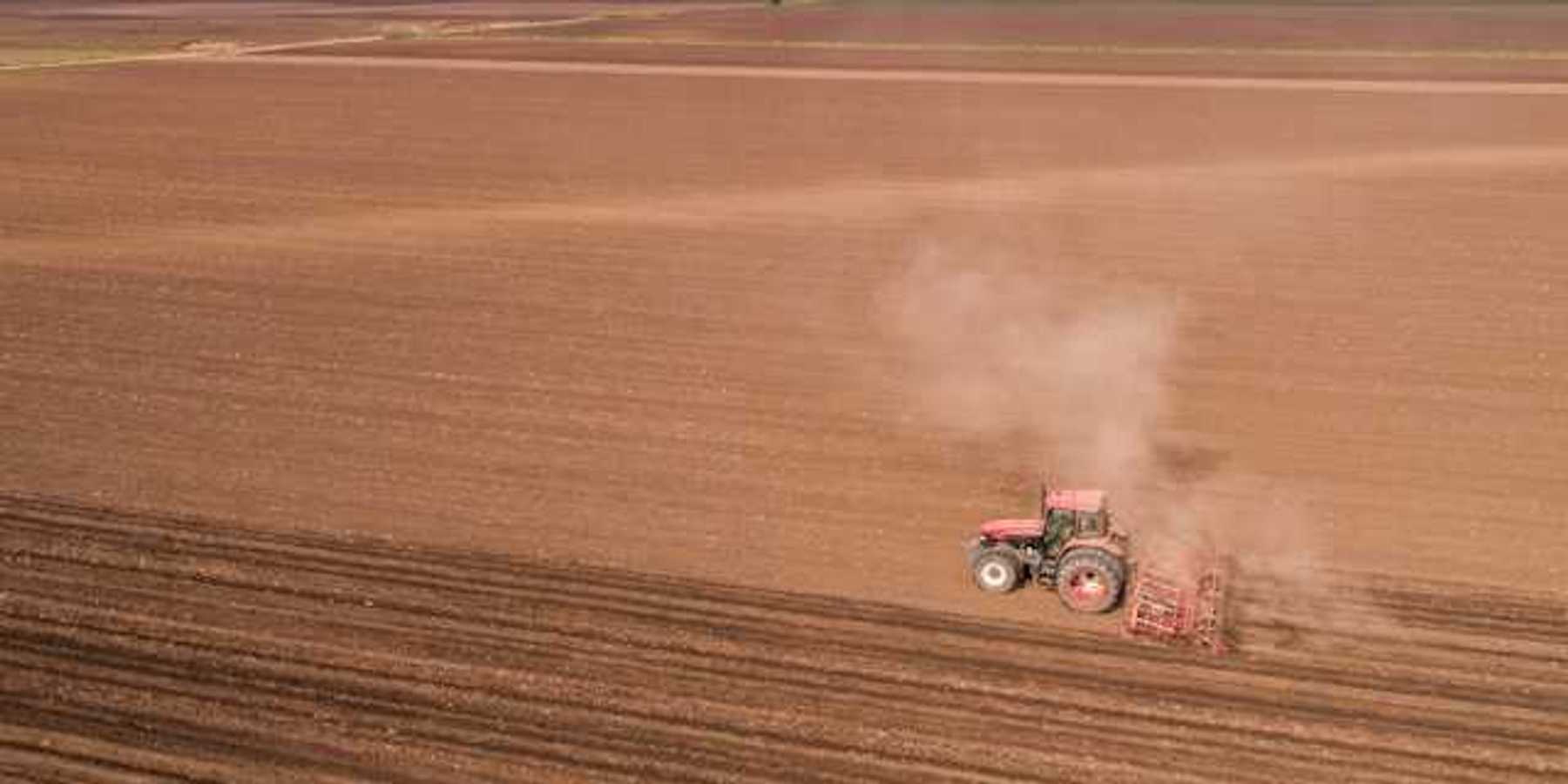 A tractor dragging an implement across a dry farm field
